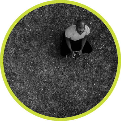 Aerial photo of site author sitting on the grass looking up at the drone taking the picture